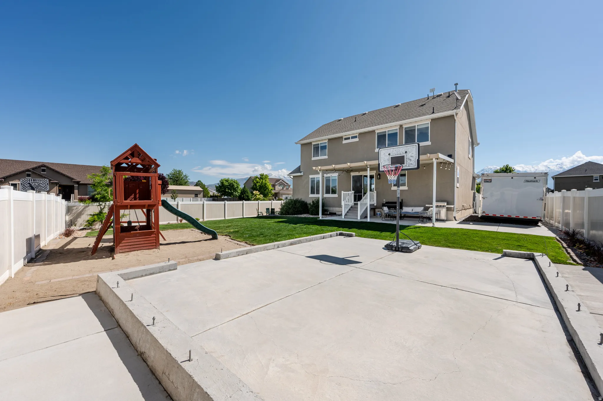 Spacious backyard featuring a large concrete patio, expansive lawn, and a light-colored privacy fence