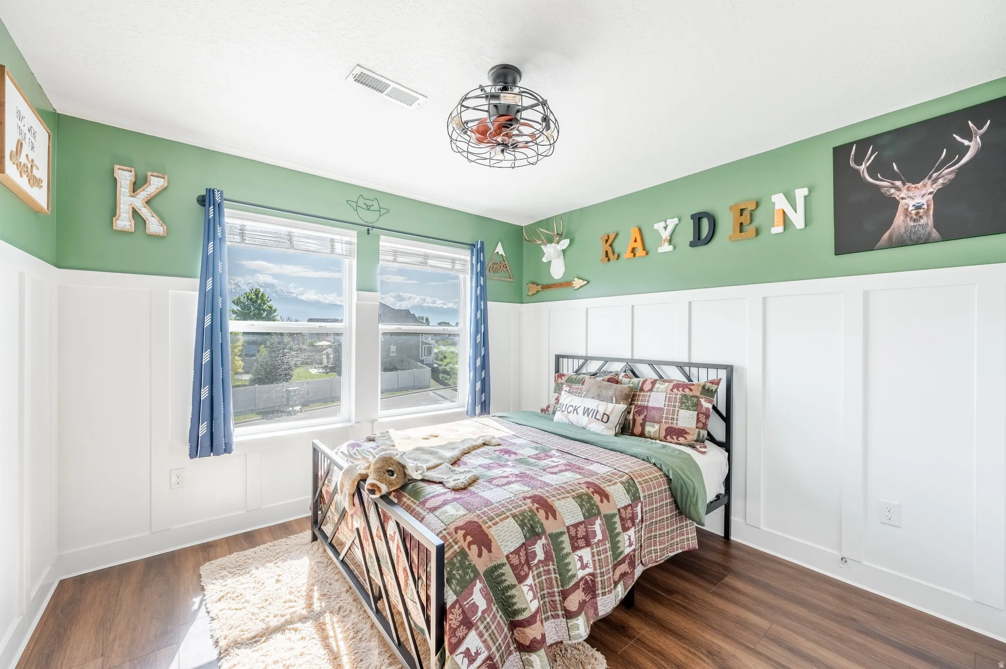 Wood-finish flooring, white wainscoting, dual windows, and an industrial-style ceiling fan