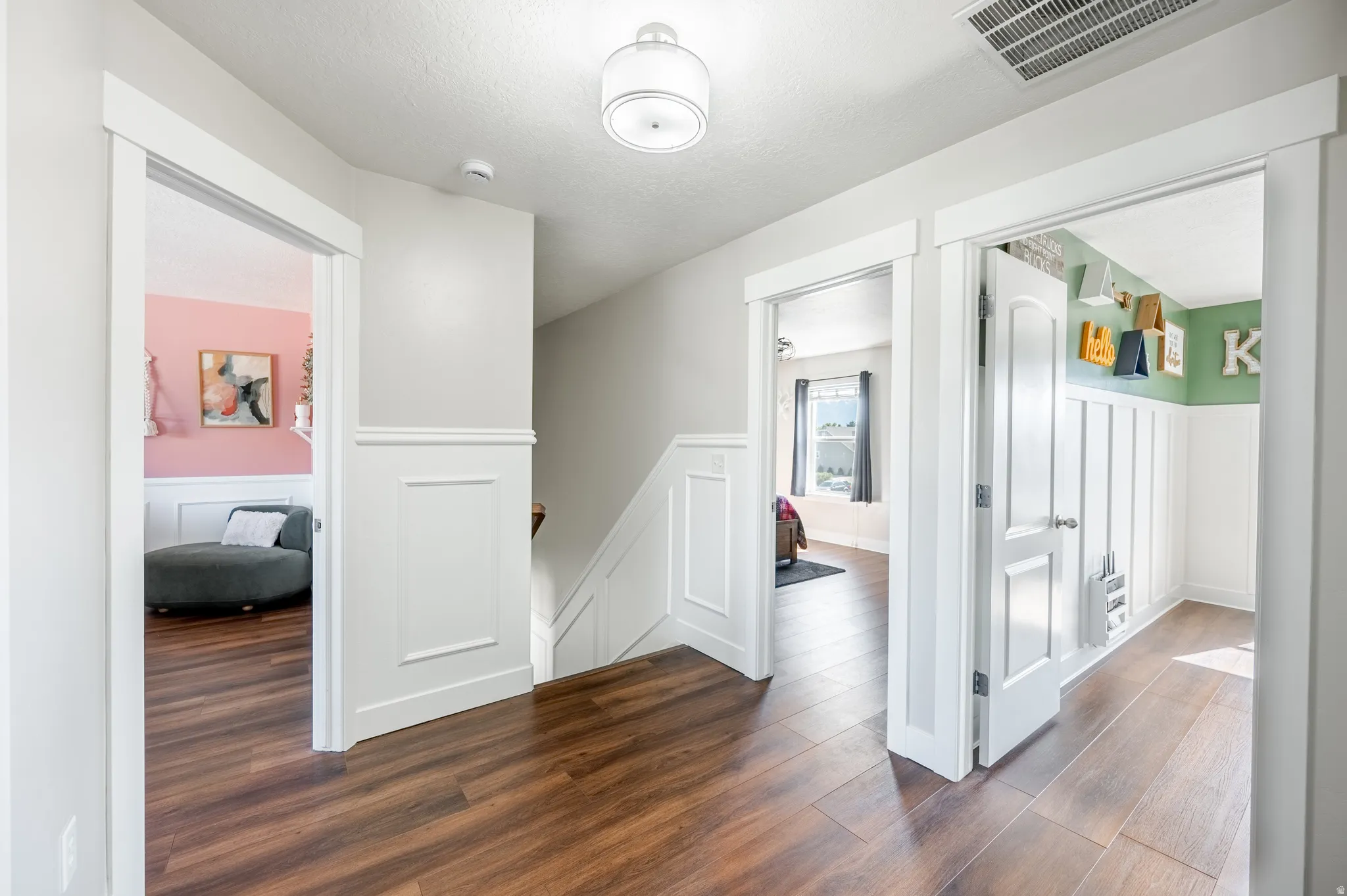 Wood-finish flooring throughout the hallway, wainscoting with decorative trim, contemporary ceiling light fixture, and white painted doors