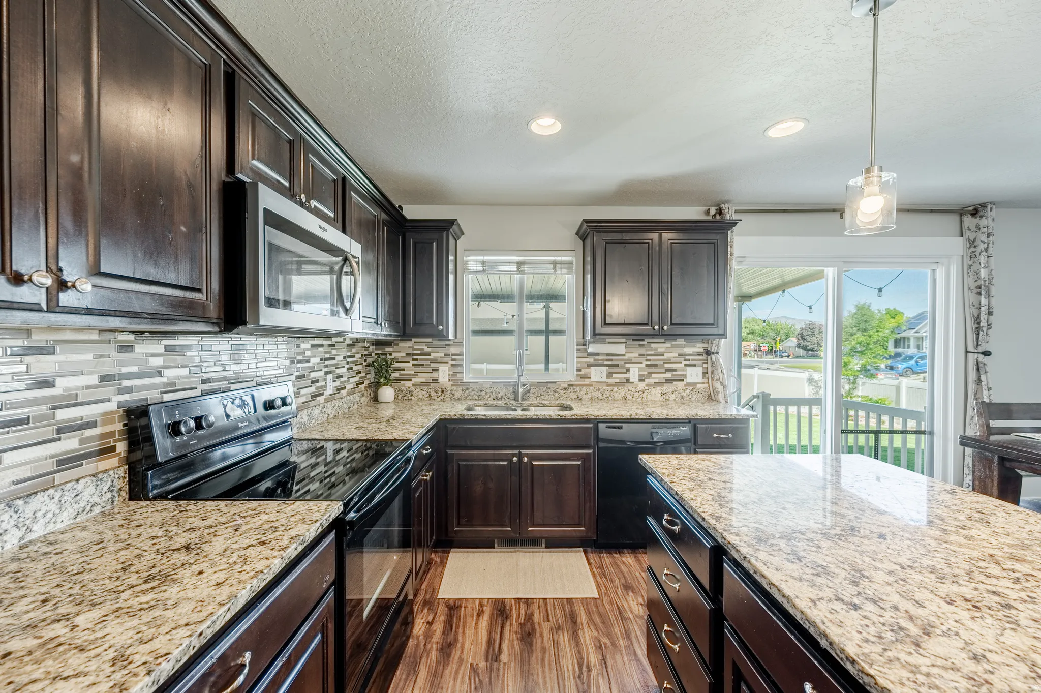 Kitchen featuring dark wood-finish cabinetry, light-toned countertops, a mosaic tile backsplash, stainless steel microwave, and wood-finish flooring