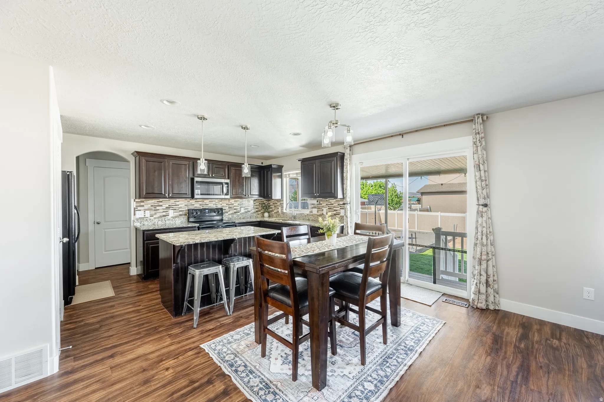Kitchen featuring dark wood-finish cabinetry, granite countertops, tile backsplash, and stainless steel appliances