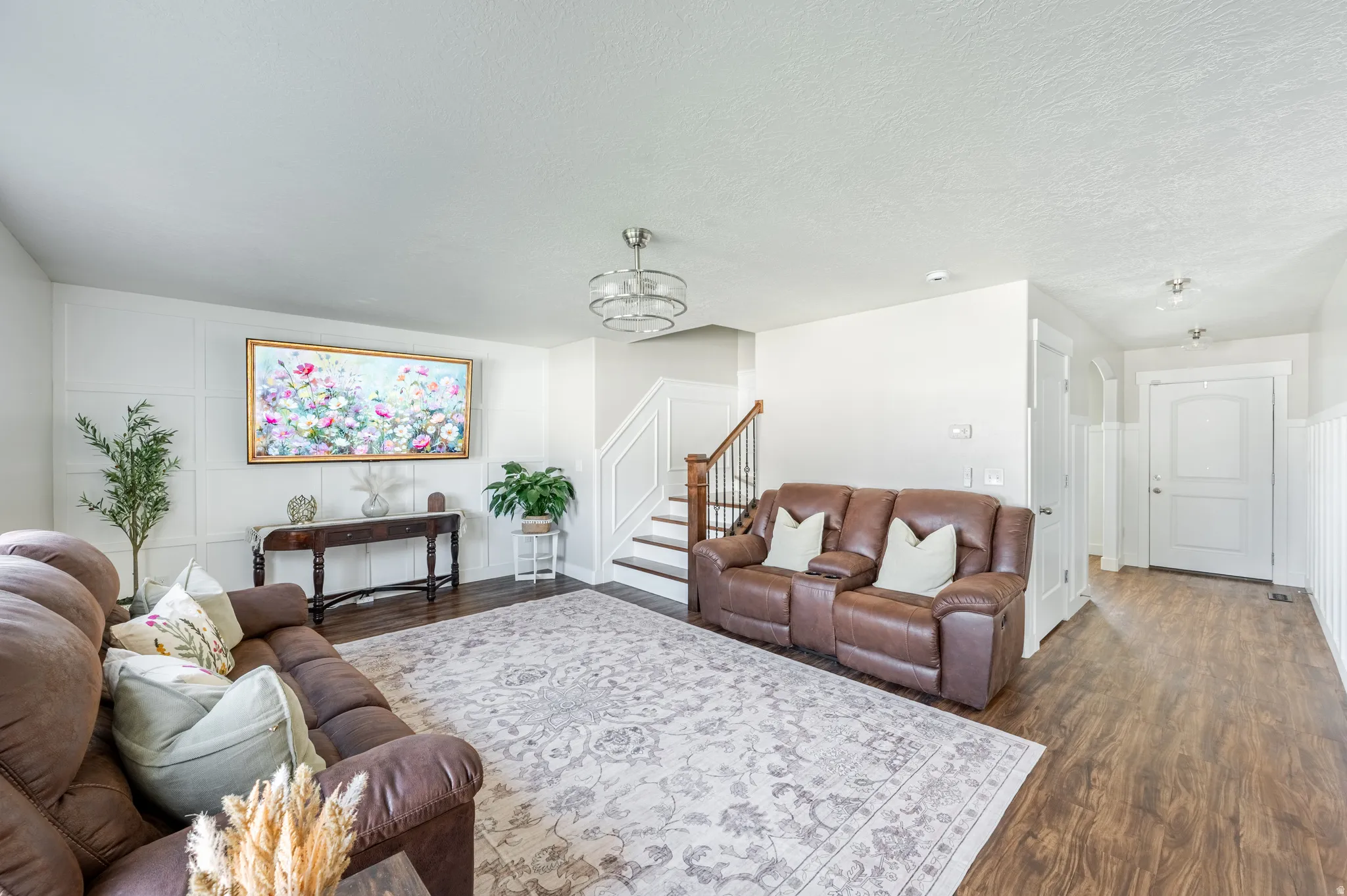 Spacious living area featuring paneling, wood-finish flooring, and a contemporary chandelier
