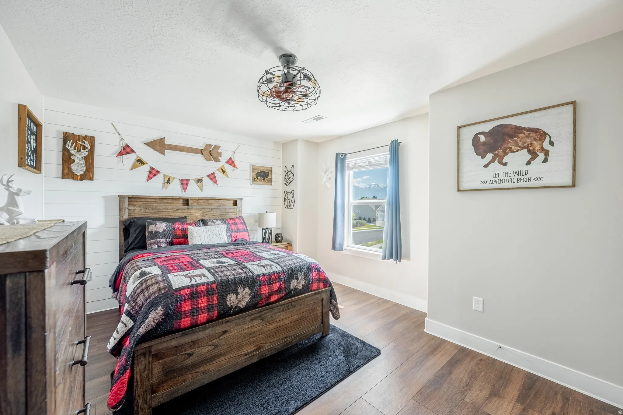 Wood-finish flooring, white shiplap accent wall, light gray painted walls, window with trim, and a ceiling fan with integrated lighting