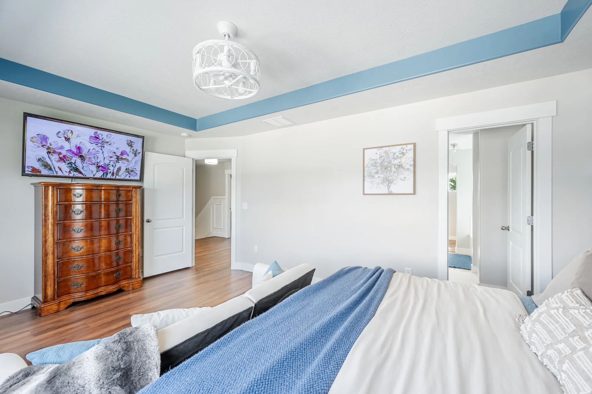 Recessed ceiling with blue trim, wood-finish flooring, white doors with modern hardware, and a decorative ceiling light fixture