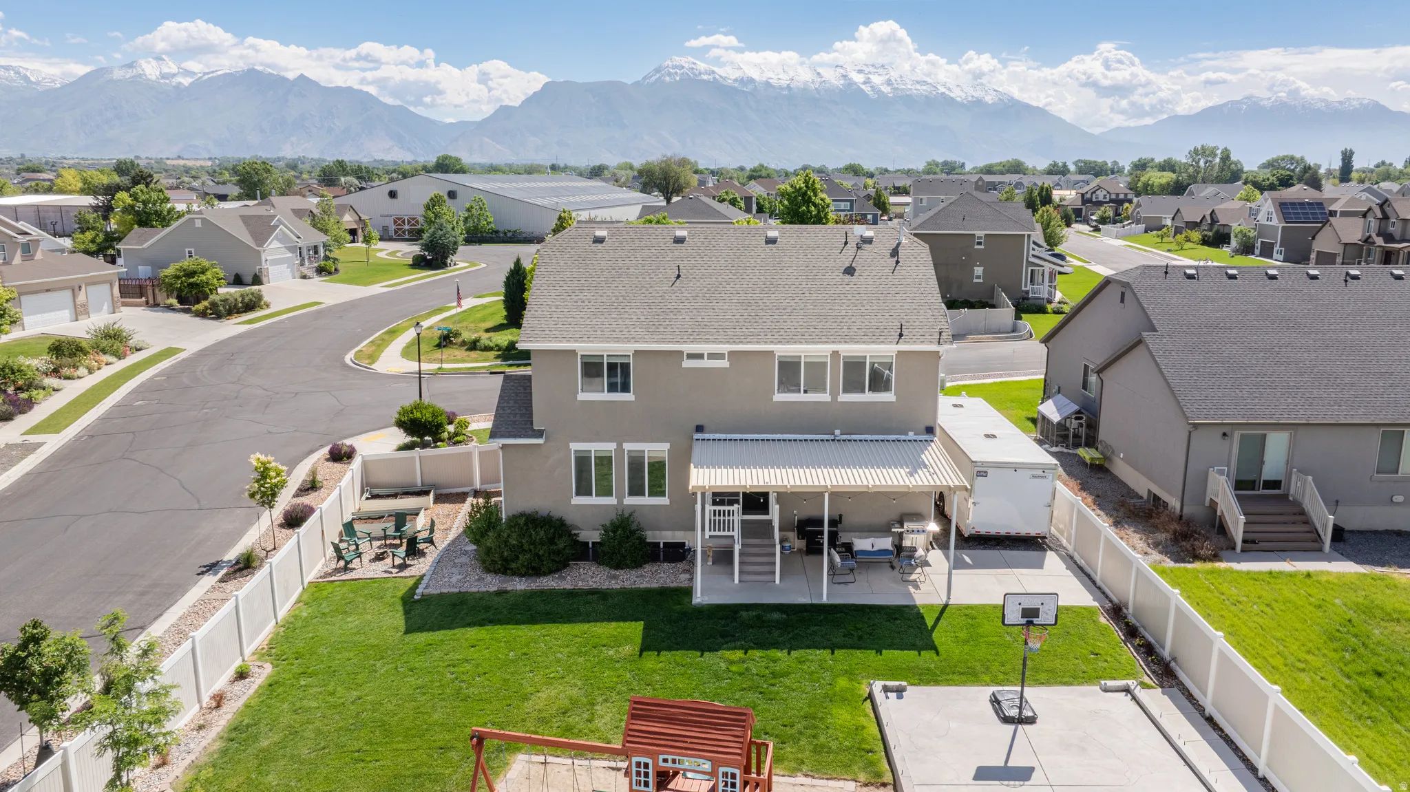 Spacious backyard featuring a covered patio, concrete sports court, and manicured lawn, enclosed by a privacy fence