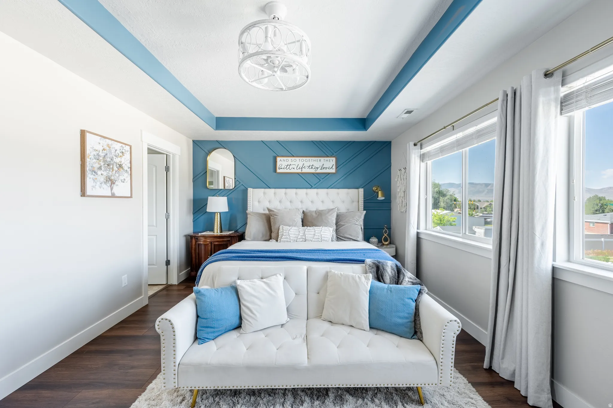 Tray ceiling, textured accent wall, dark wood-finish flooring, recessed lighting, and multiple windows