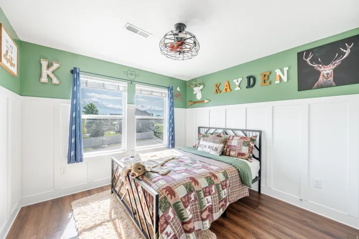 Wood-finish flooring, white wainscoting, dual windows, and an industrial-style ceiling fan