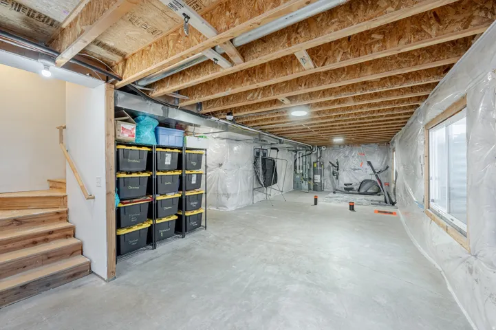 Unfinished basement with exposed wood joists, concrete flooring, and a large window
