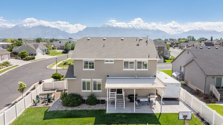 Back exterior featuring a covered patio, expansive lawn area, and white vinyl fencing