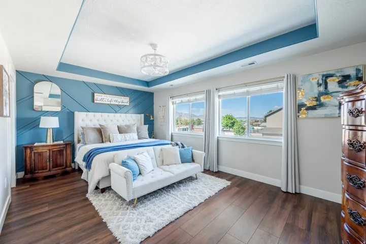 Tray ceiling with accent paint, wood-finish flooring, two large windows, accent wall with geometric paneling