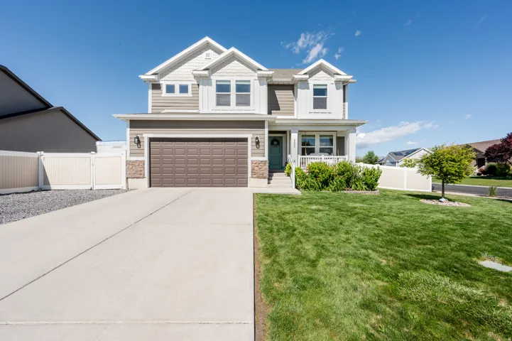 Contemporary two-story residence featuring a two-car garage, stone and siding exterior, front porch with white railings, mature landscaping, and a concrete driveway