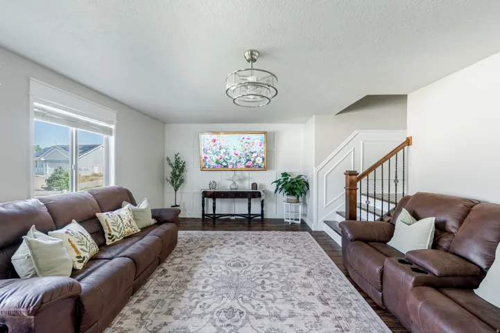 Spacious living area featuring wood-finish flooring, a contemporary chandelier, and a prominent staircase with wood newel posts and wrought iron balusters