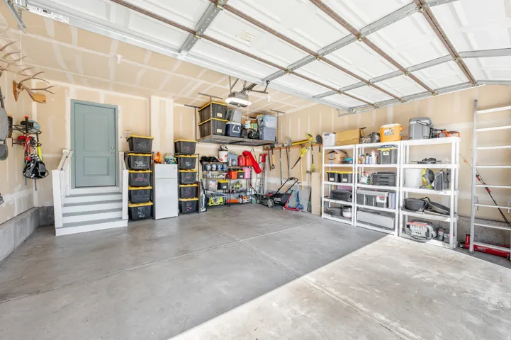 Concrete floor garage with a light-colored entry door, interior steps, and elevated storage