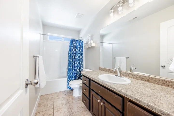 Ceramic tile flooring, white porcelain bathtub, single vanity with integrated sink, dark wood-finish cabinetry, and stone-finish countertop
