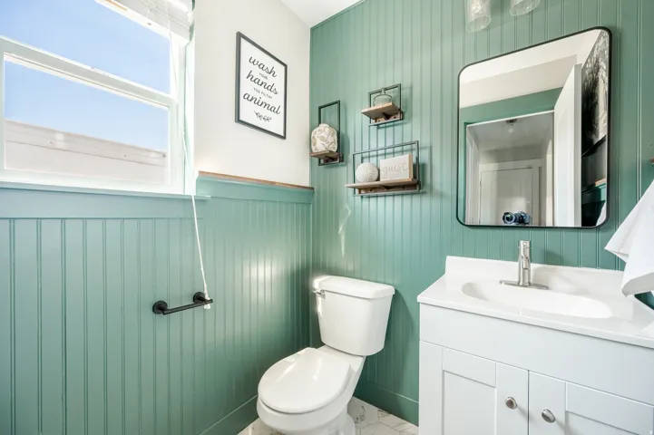 Bathroom featuring beadboard wainscoting, a single-pane window, a white vanity with an integrated sink, a rectangular framed mirror, and hexagonal floor tiling