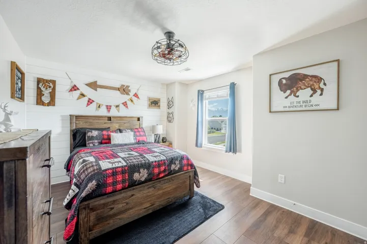Wood-finish flooring, white shiplap accent wall, light gray painted walls, window with trim, and a ceiling fan with integrated lighting