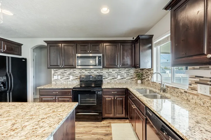 Kitchen featuring dark wood-finish cabinetry, granite countertops, tile backsplash, stainless steel microwave, and wood-finish flooring