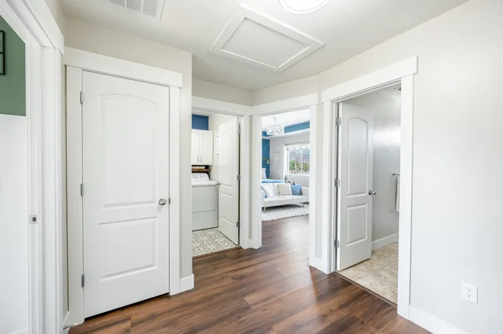 Wood-finish flooring throughout, white trim and doors, laundry area with built-in cabinetry, additional room with white walls and blue accent wall, bathroom with tiled flooring
