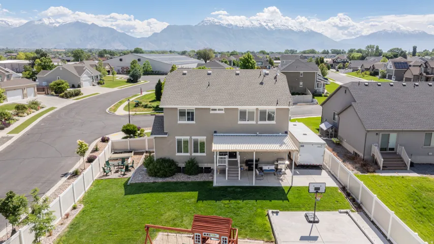 Spacious backyard featuring a covered patio, concrete sports court, and manicured lawn, enclosed by a privacy fence