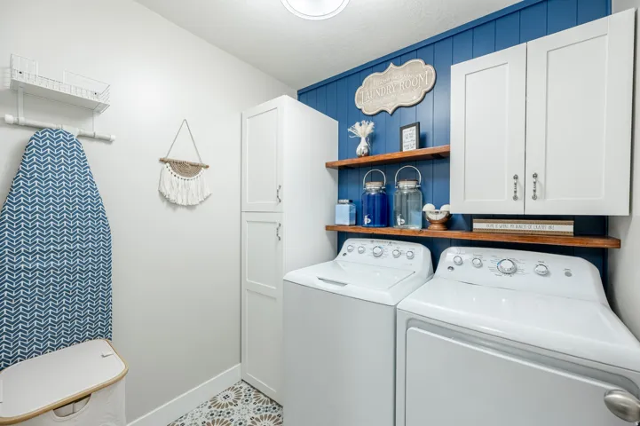 Laundry area featuring white cabinetry, wood-finish shelving, blue shiplap paneling, and patterned floor tile