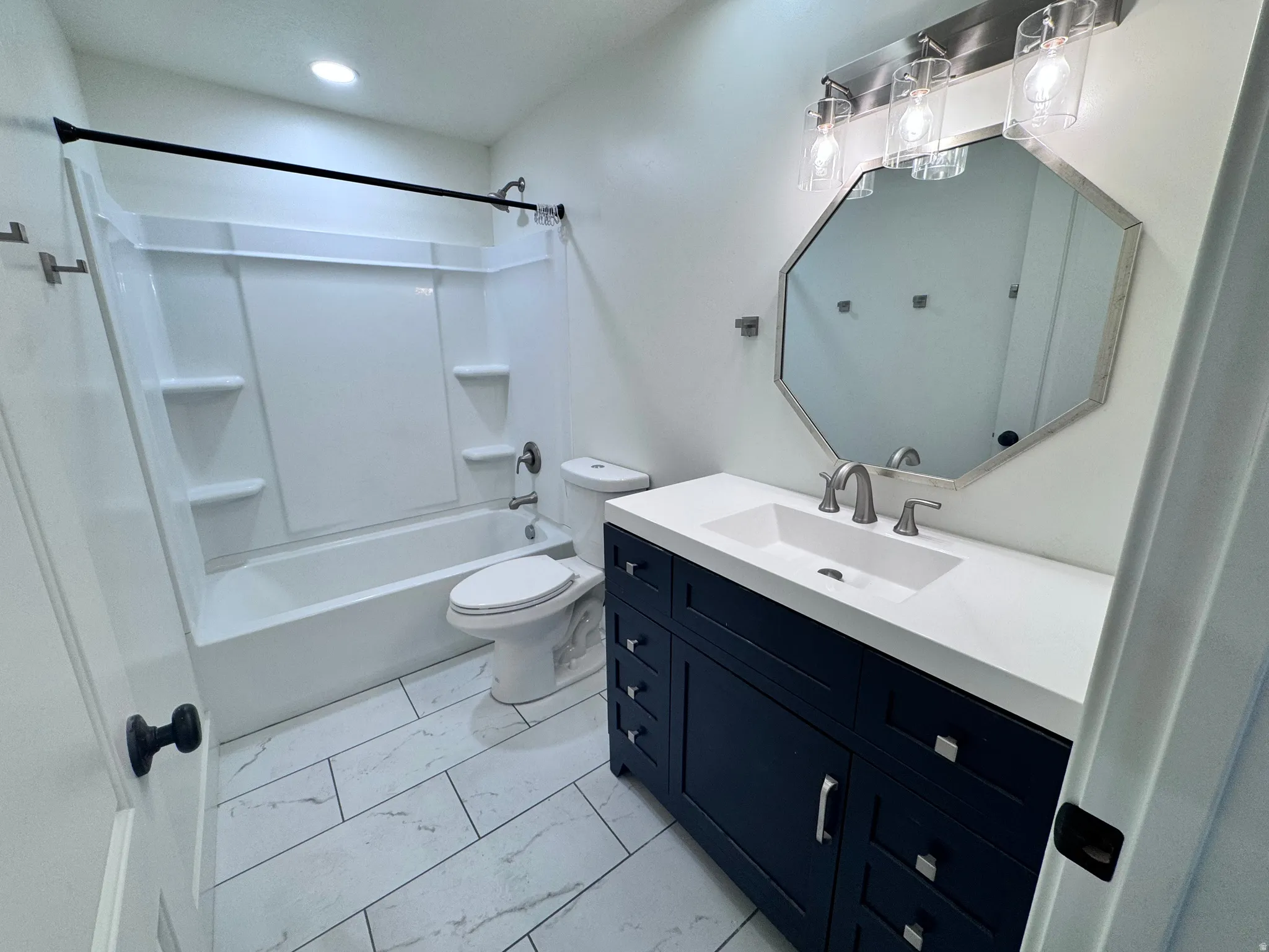 Bathroom featuring a dark blue vanity with silver hardware, an integrated white sink, and a coordinating octagonal mirror
