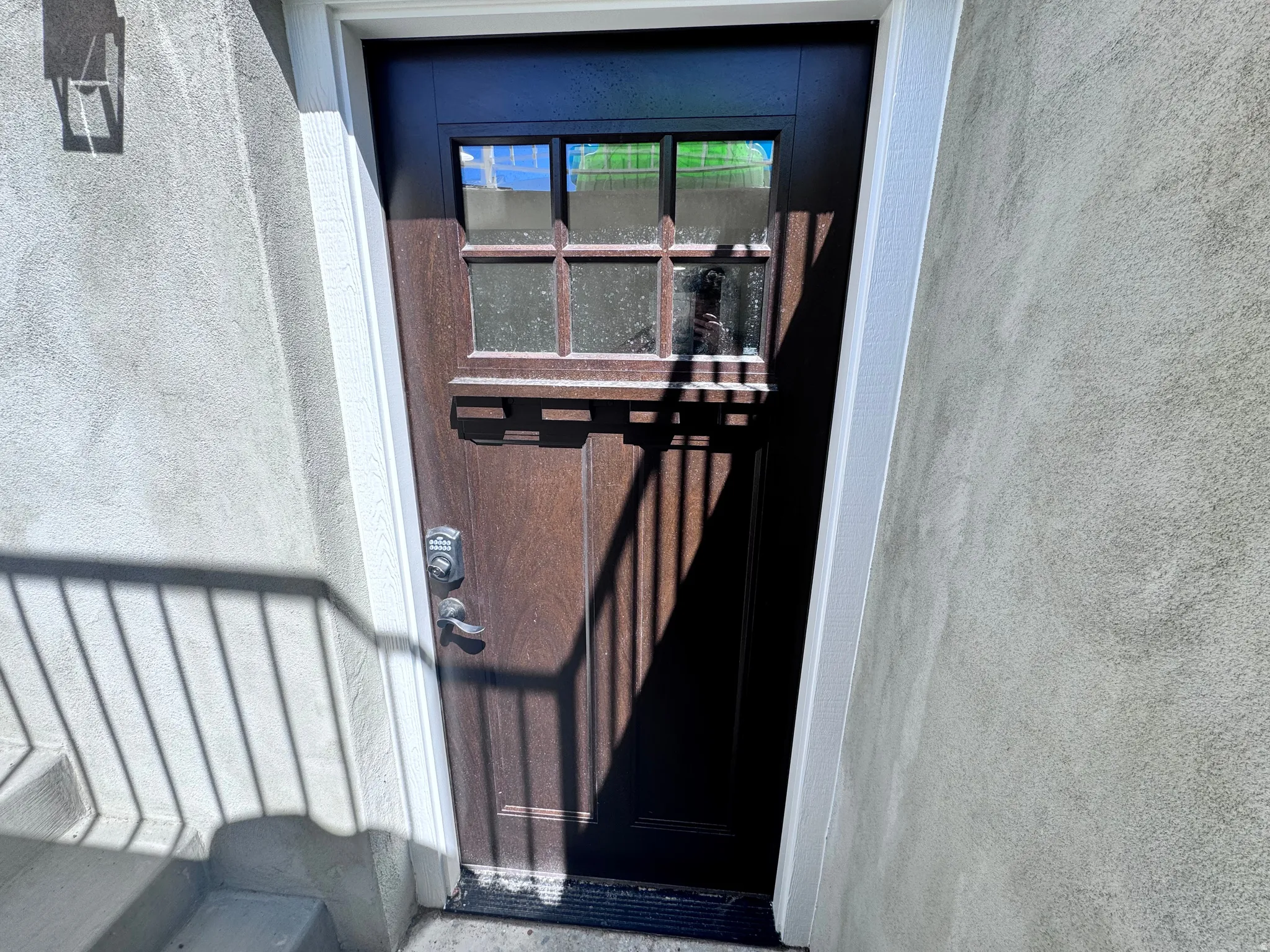 Dark wood-finish entry door with multi-pane glass insert, contrasting white trim, and a keyless entry system