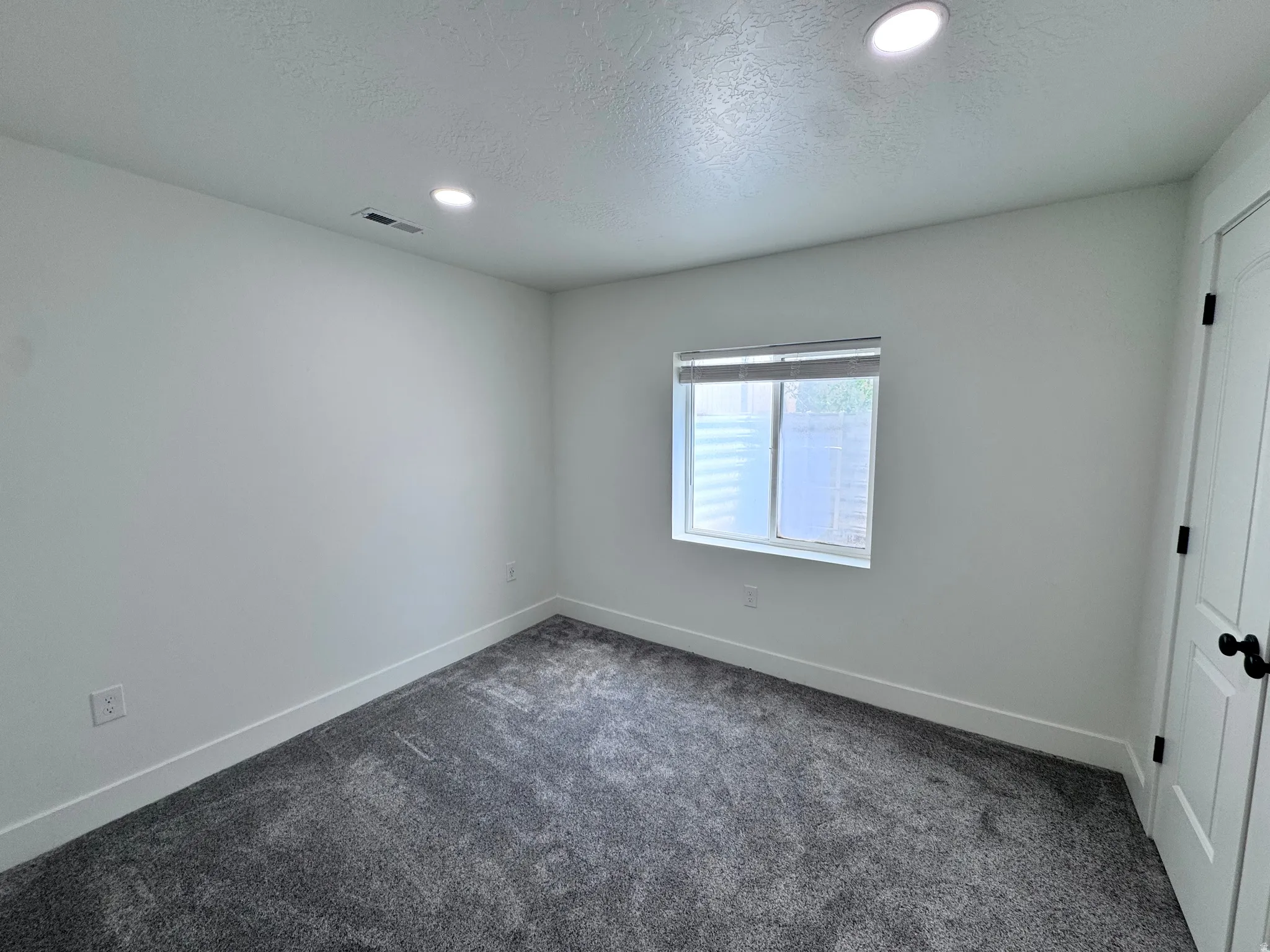 White-painted room featuring recessed lighting, a window with blinds, and dark grey carpeting