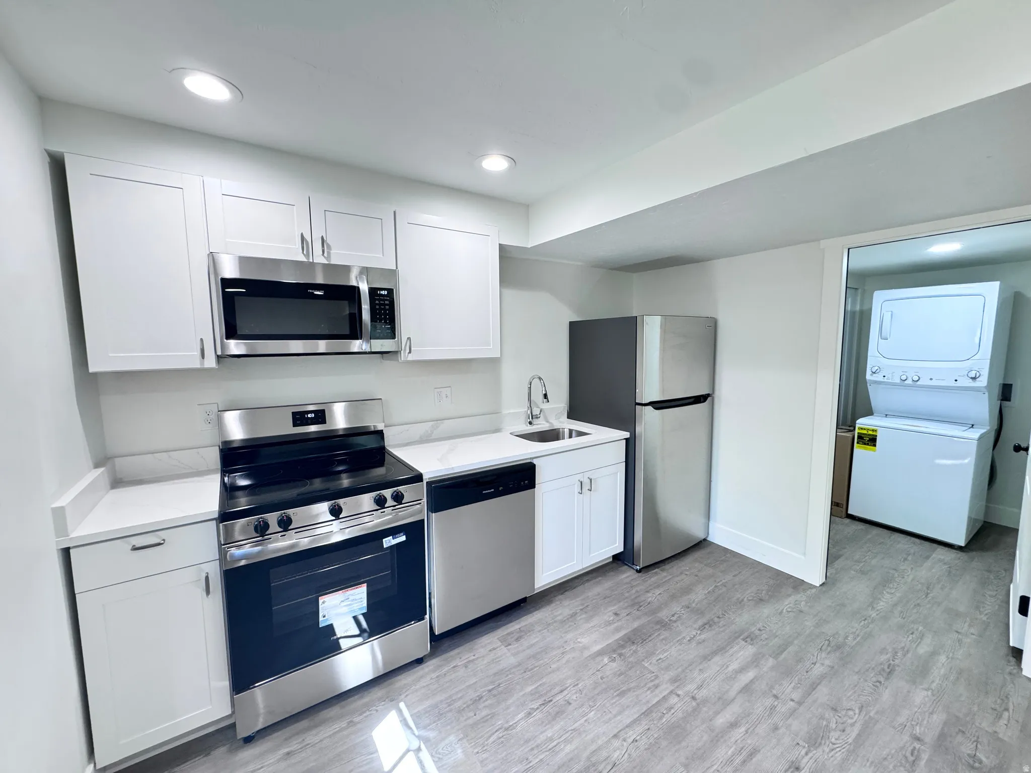 Modern kitchen featuring white shaker cabinetry, stainless steel appliances, white countertops with a matching backsplash, recessed lighting, and wood-finish flooring