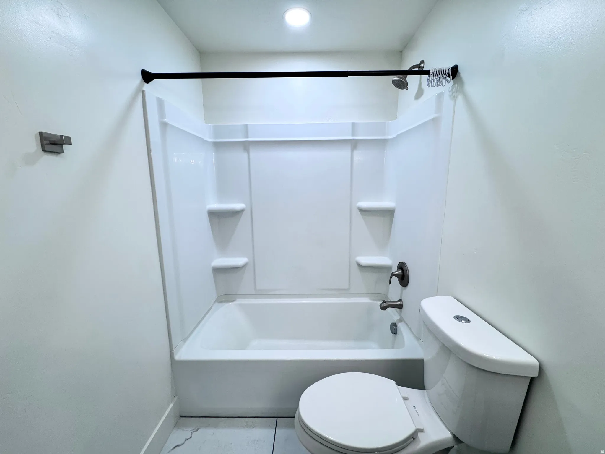 White bathtub with integrated shelving, brushed bronze fixtures, and a coordinating shower curtain rod