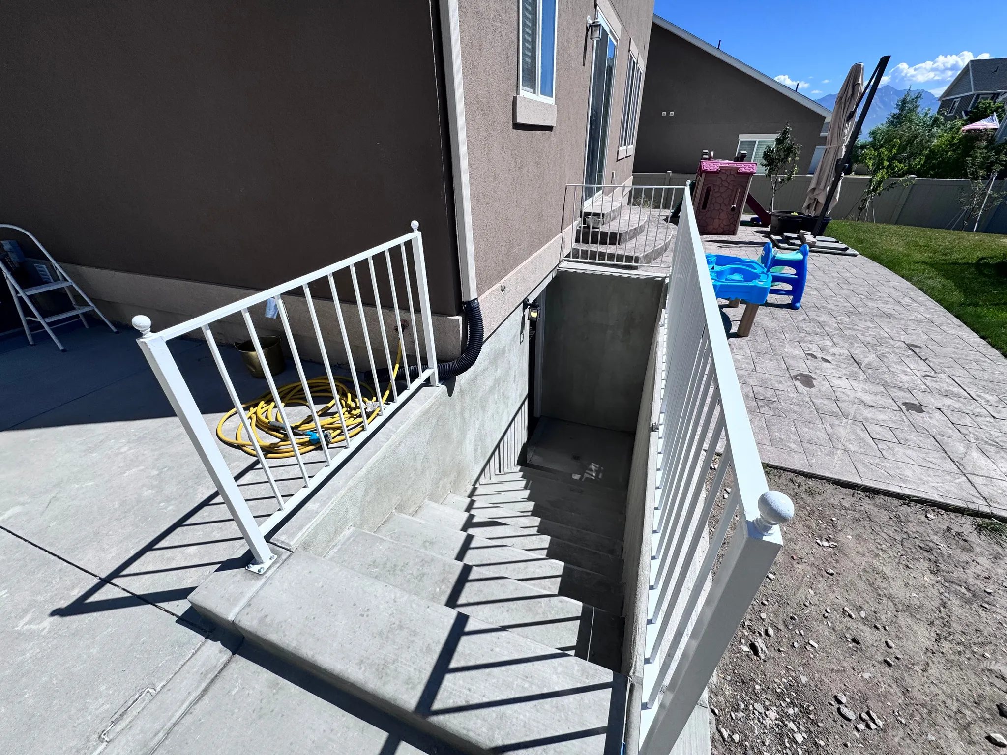 Exterior basement entry featuring concrete stairs and white metal railings