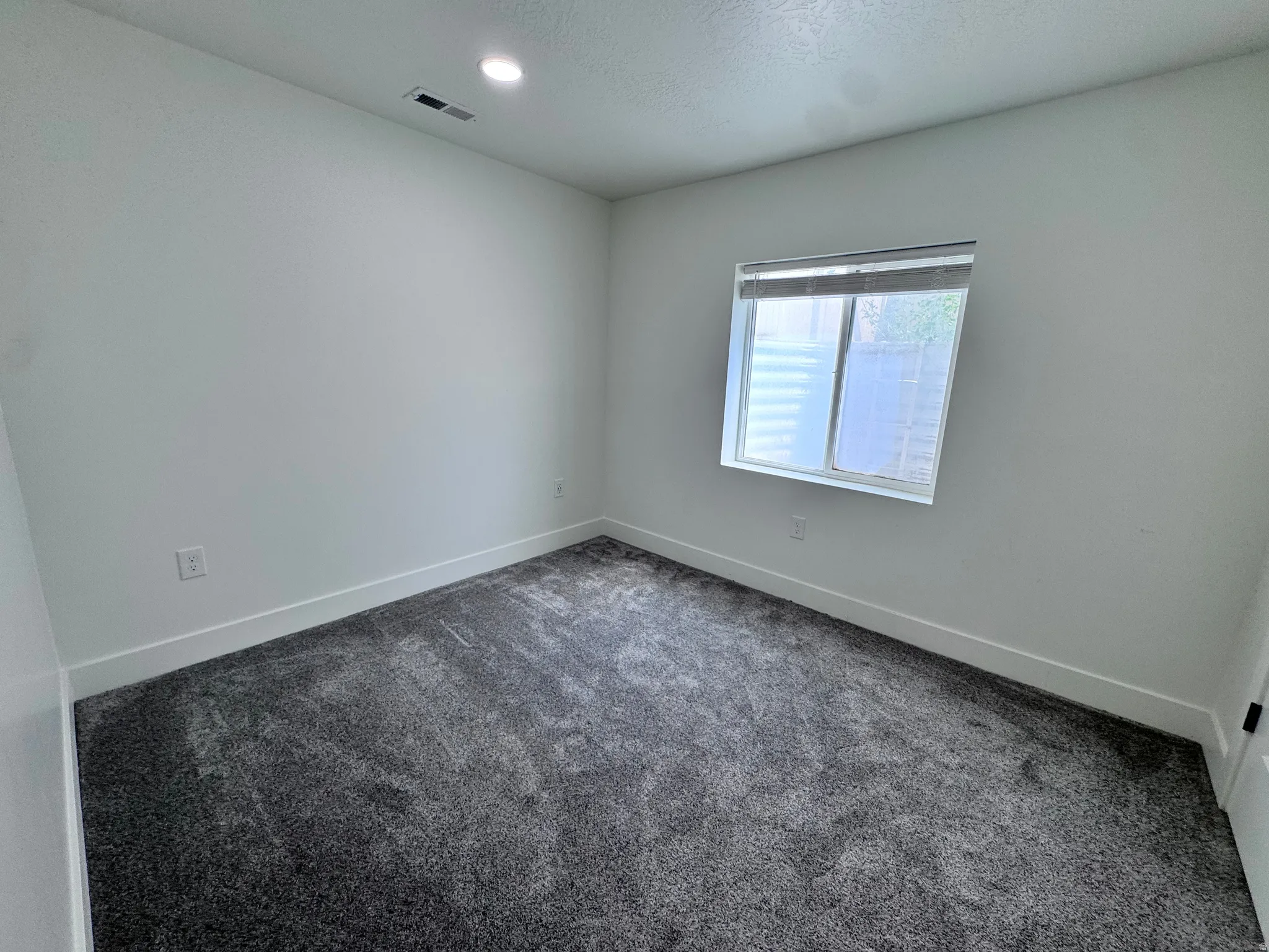 Bedroom featuring light gray walls, dark gray carpet, a single window with blinds, and recessed lighting