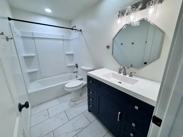 Bathroom featuring a dark blue vanity with silver hardware, an integrated white sink, and a coordinating octagonal mirror