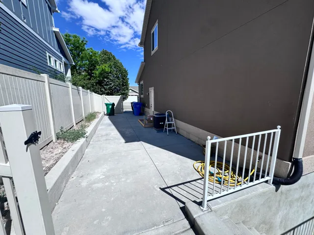 Side concrete patio with a white metal railing, a solid privacy fence, and a stucco exterior
