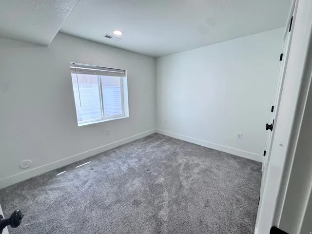 Neutral-toned room featuring a single window with blinds, recessed lighting, and gray carpeting