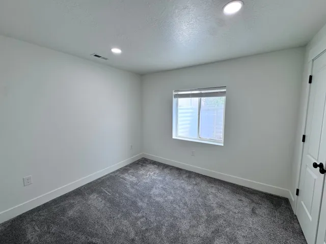 White-painted room featuring recessed lighting, a window with blinds, and dark grey carpeting