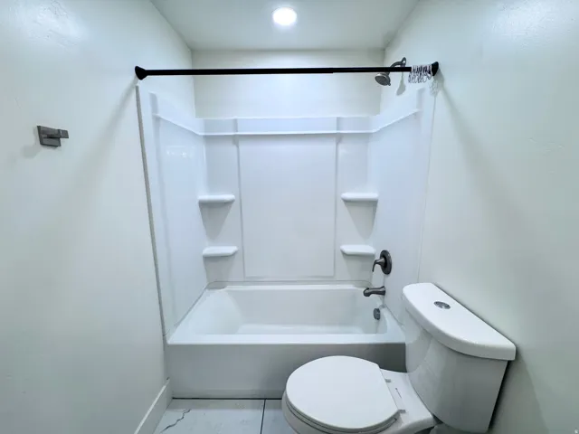 White bathtub with integrated shelving, brushed bronze fixtures, and a coordinating shower curtain rod