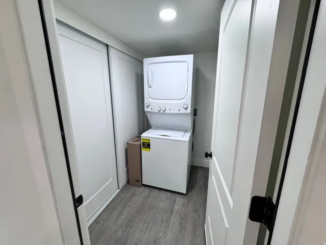 Dedicated laundry space featuring a stacked washer and dryer unit, wood-finish flooring, and bright overhead lighting