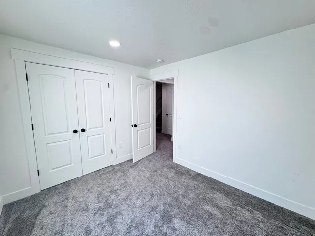 Spacious room featuring plush gray carpeting, white walls, white trim, recessed lighting, and a double-door closet with matte black hardware