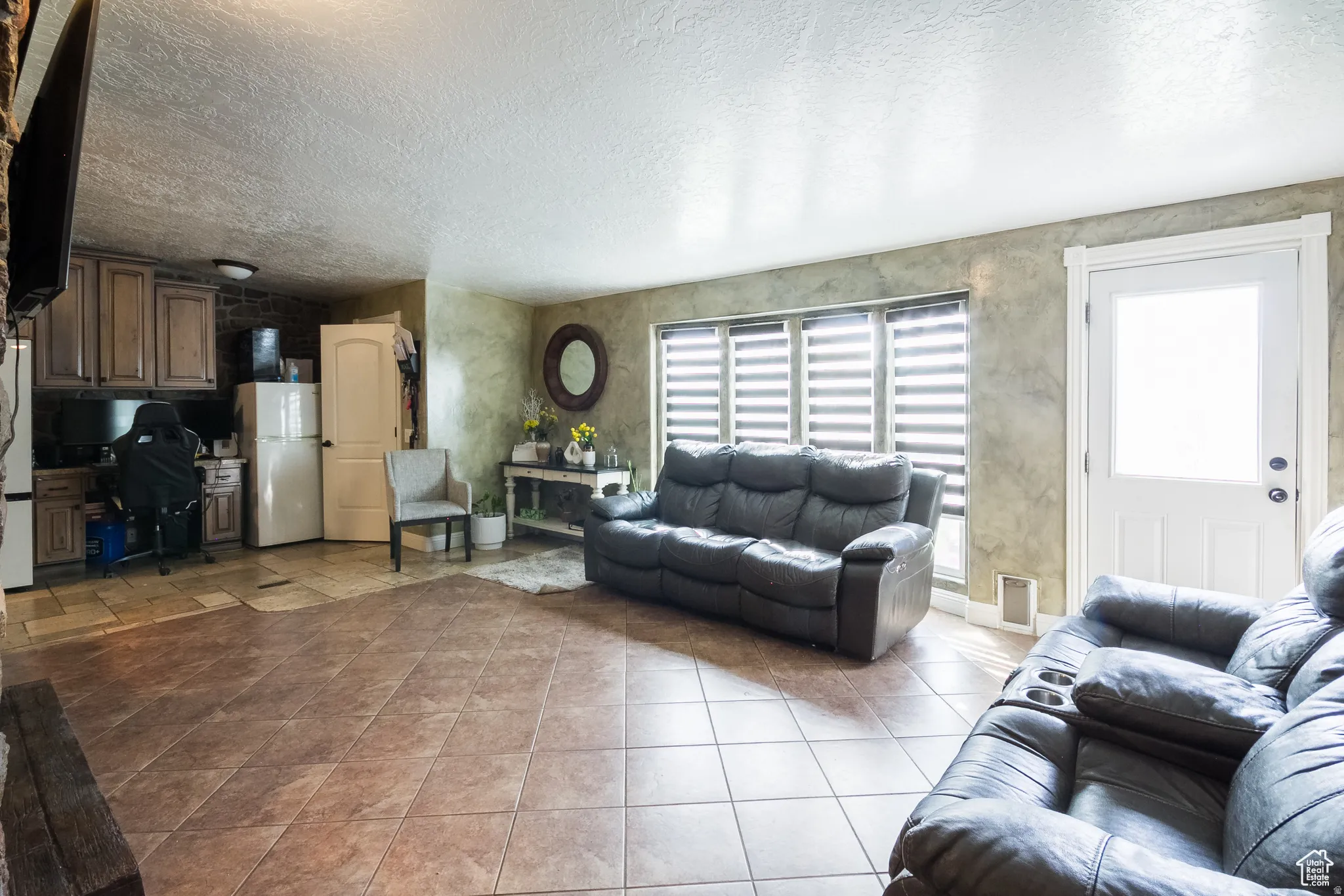 Spacious interior featuring large format tile flooring, a white paneled door with frosted glass, and multiple windows with horizontal blinds