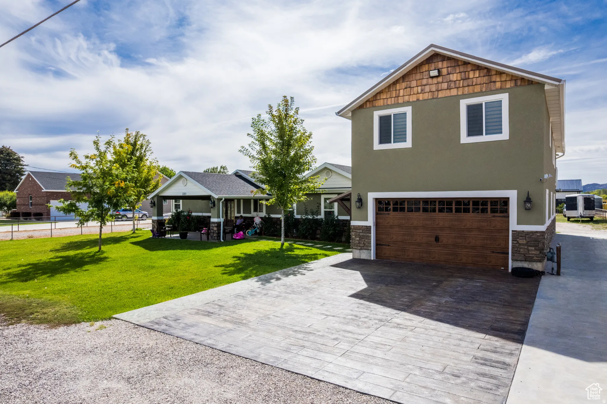 Two-story structure featuring a wood-finish garage door, stone veneer accents, and upper-level windows
