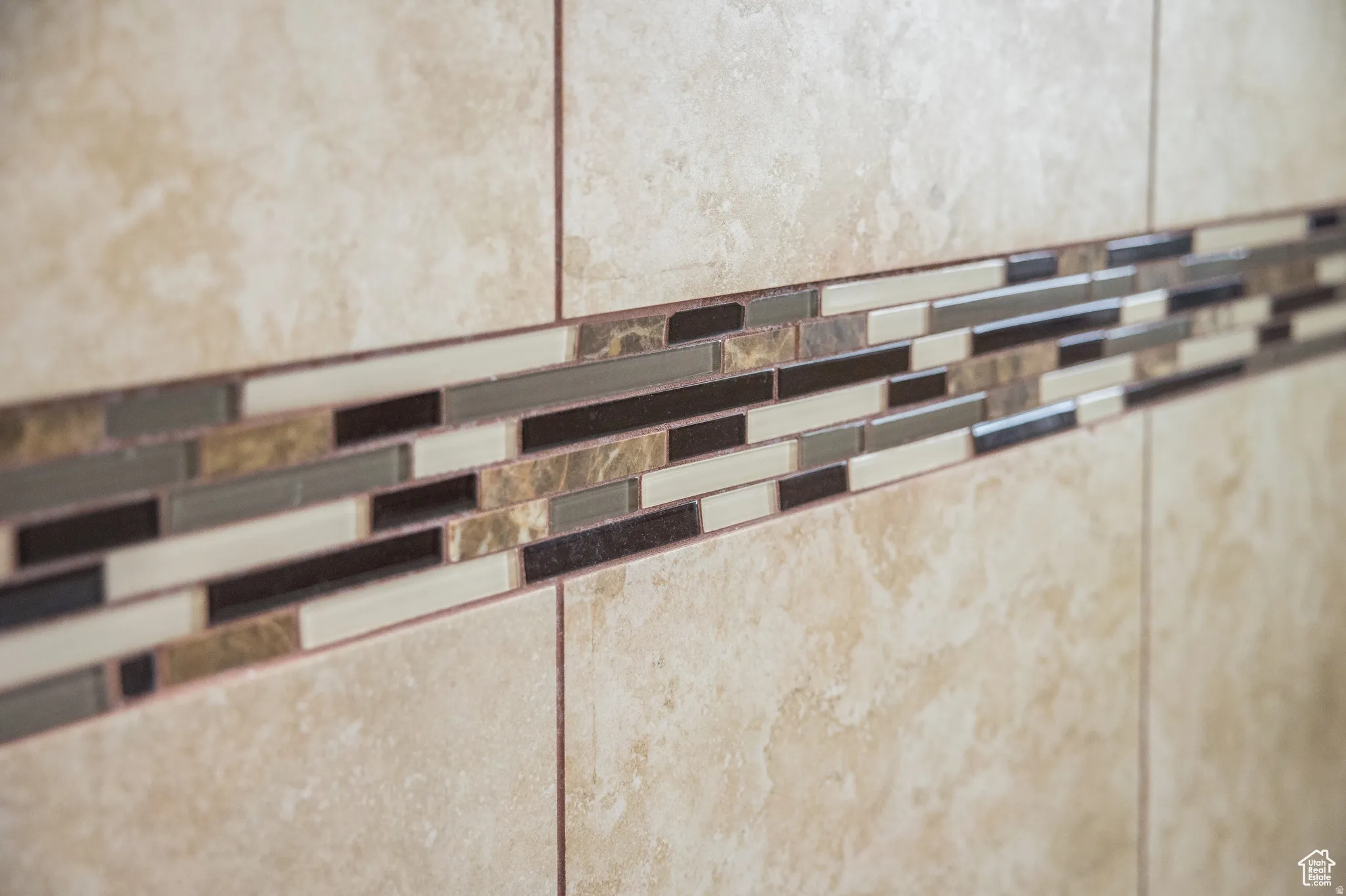 Large format beige wall tile with a mosaic accent band featuring varied rectangular tiles in earth tones