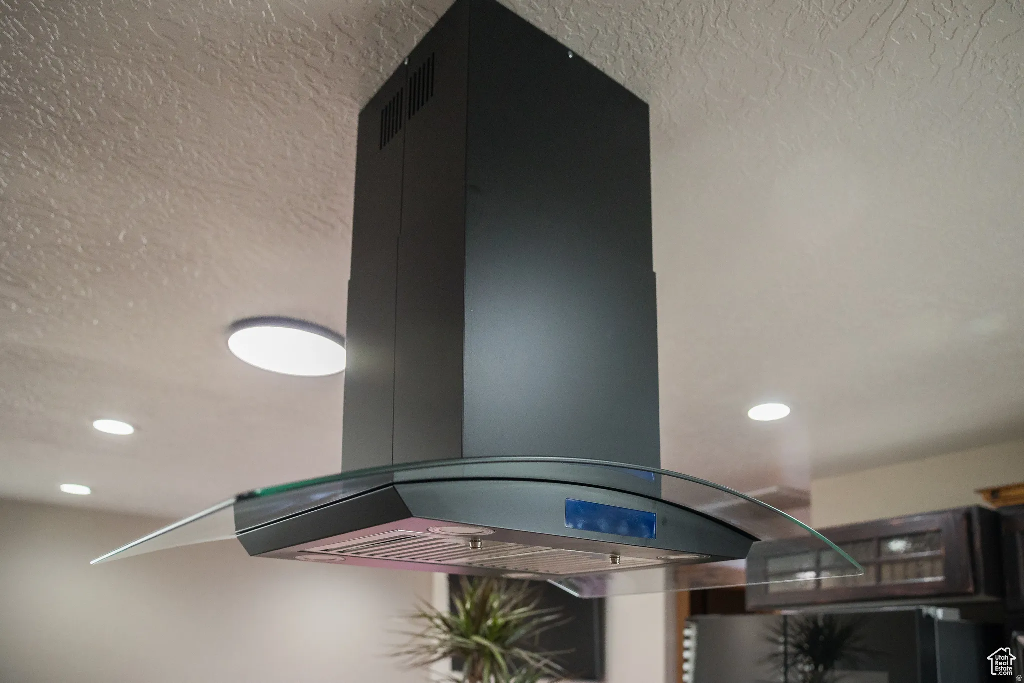 Modern island range hood with a curved glass canopy, metallic finish, and task lighting