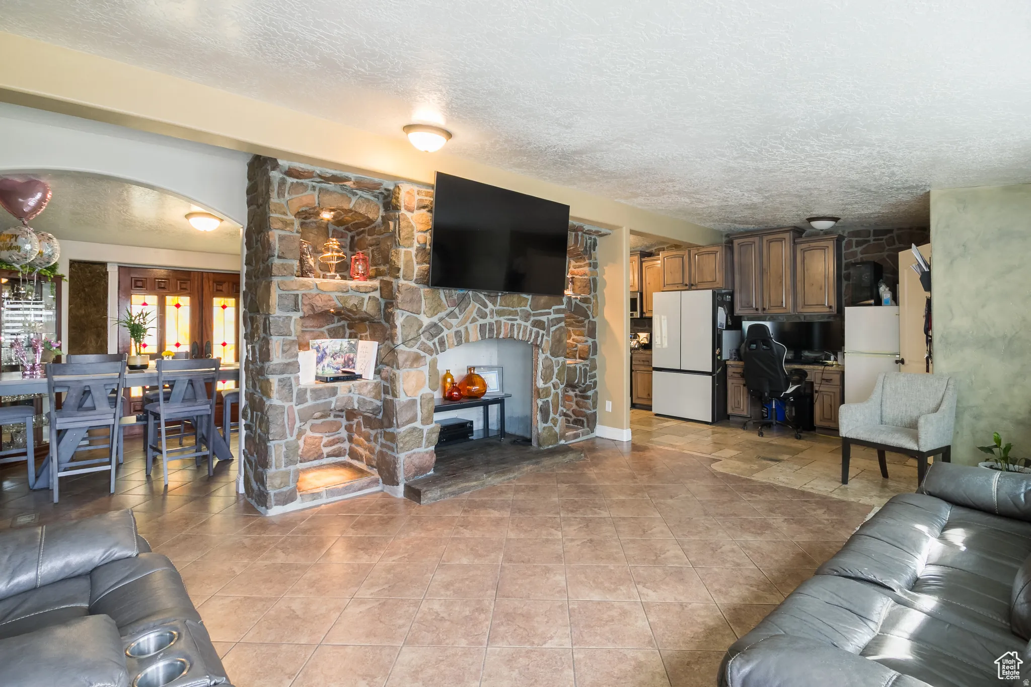Stone fireplace with hearth, tile flooring, built-in kitchen cabinetry, arched entryway, and recessed lighting