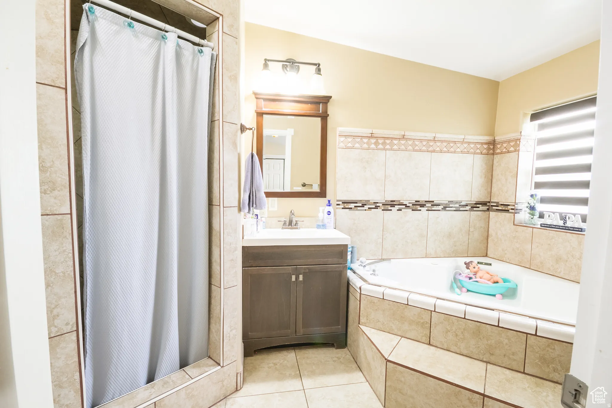 Bathroom featuring a corner soaking tub with tiled surround, a separate tiled shower, and a wood-finish vanity with an integrated sink and wall-mounted mirror