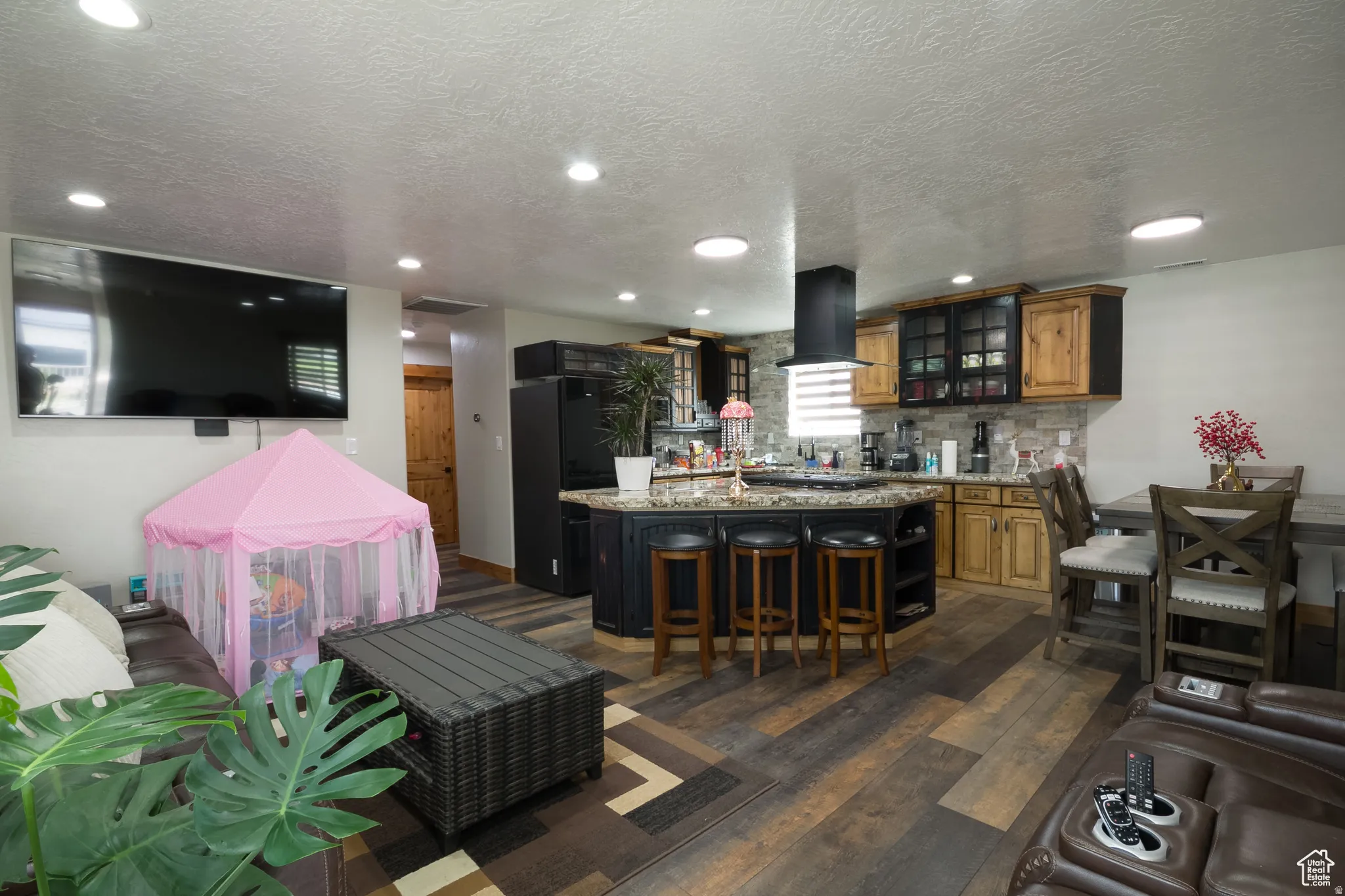 Open-concept living space featuring wood-finish flooring, recessed lighting, and a kitchen with an island, dark cabinetry, and light wood-tone upper cabinets