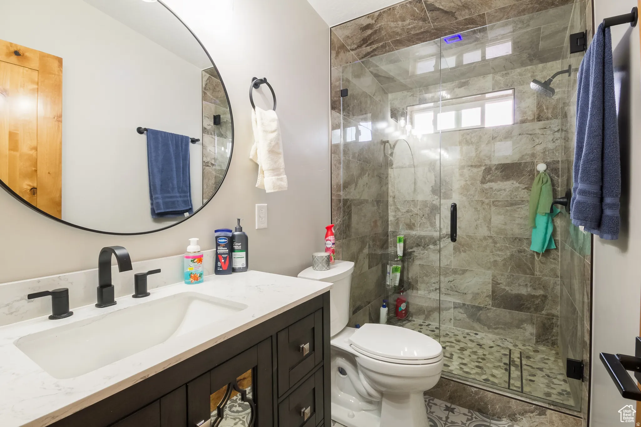 Modern bathroom featuring a dark wood-finish vanity with a white countertop and integrated rectangular sink, matte black faucet, and a round wall mirror