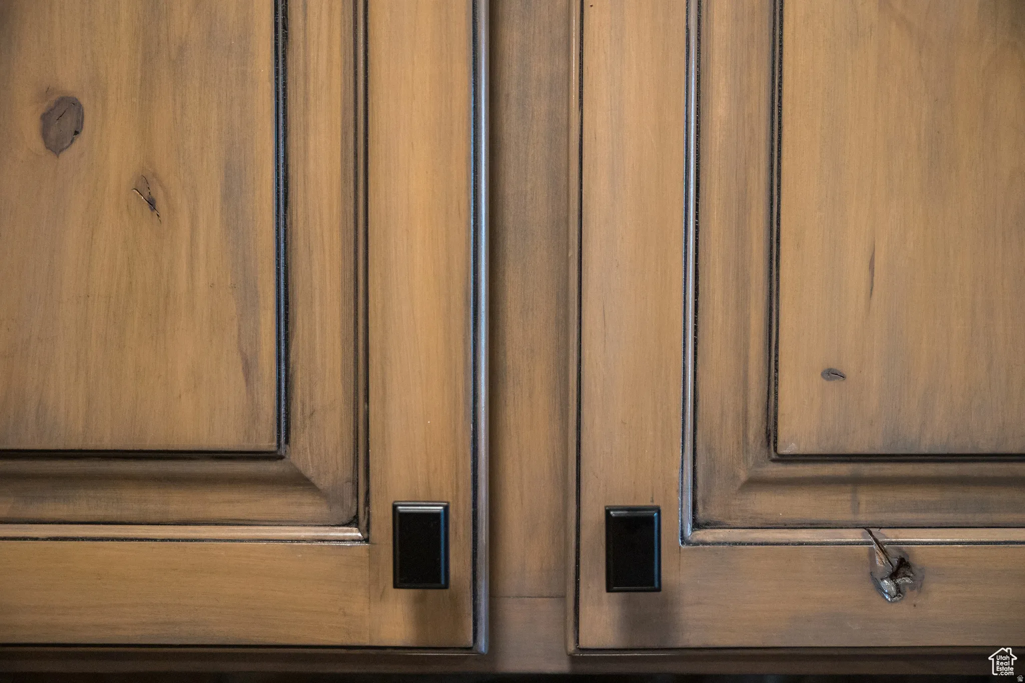 Wooden cabinetry featuring a distressed finish, raised panel doors, and black rectangular hardware
