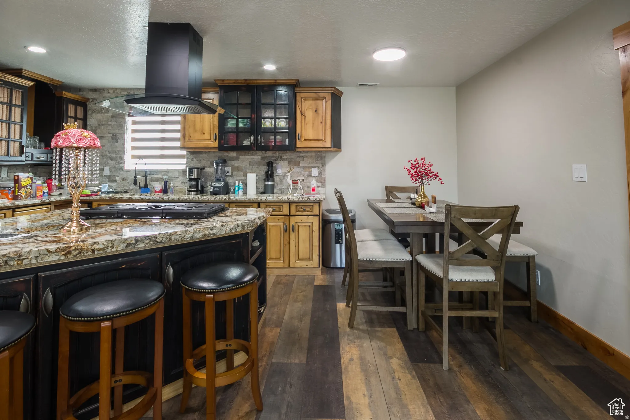 Kitchen featuring an island with stone-finish countertop, dark cabinetry, and integrated cooktop
