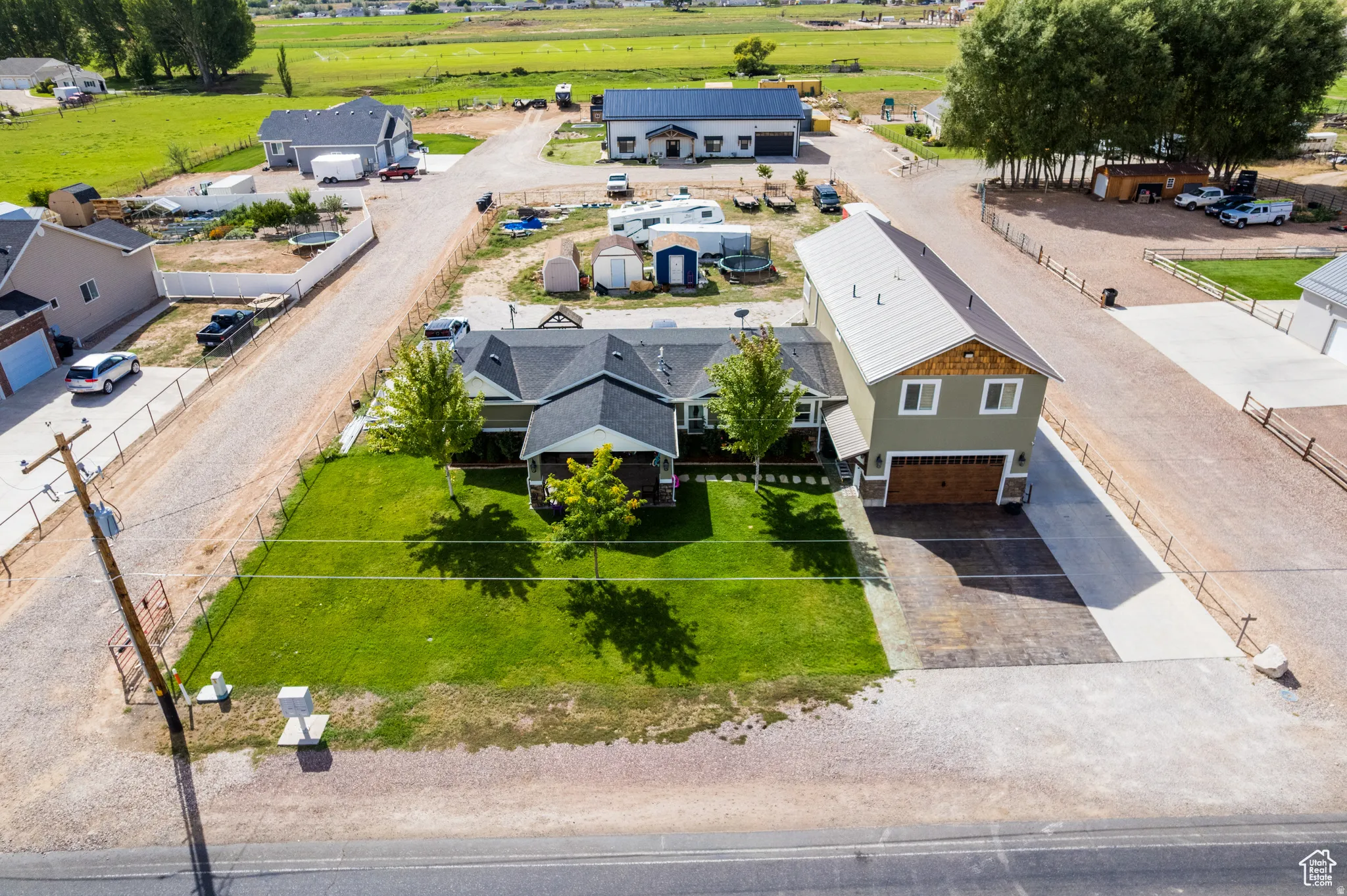 Expansive property featuring a main residence with a covered porch, a detached multi-story auxiliary building with a wood-finish garage door, a substantial gravel driveway, and a manicured front lawn