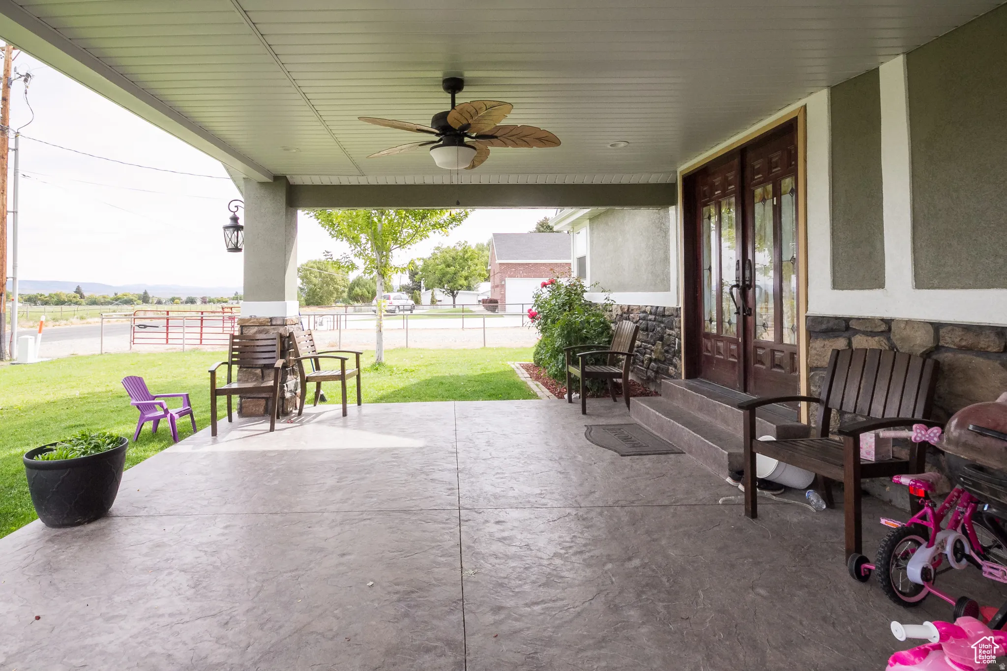 Spacious covered porch with stamped concrete flooring, equipped with a ceiling fan and an exterior lantern fixture